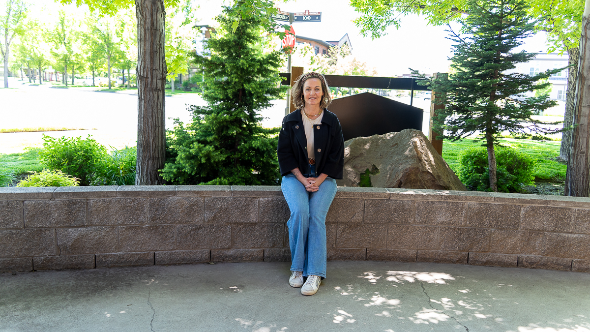 Comprehensive Guide to Porcelain Veneers in Bend, Oregon 1 A woman sits on a stone wall in a shaded outdoor area with trees and greenery in the background.