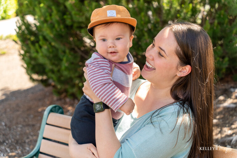 A woman sitting on a bench outdoors holds a smiling baby wearing a striped shirt and brown hat, sharing a moment as they enjoy the sunshine—an image reflecting the joy holistic approaches to dental care can bring to family life.