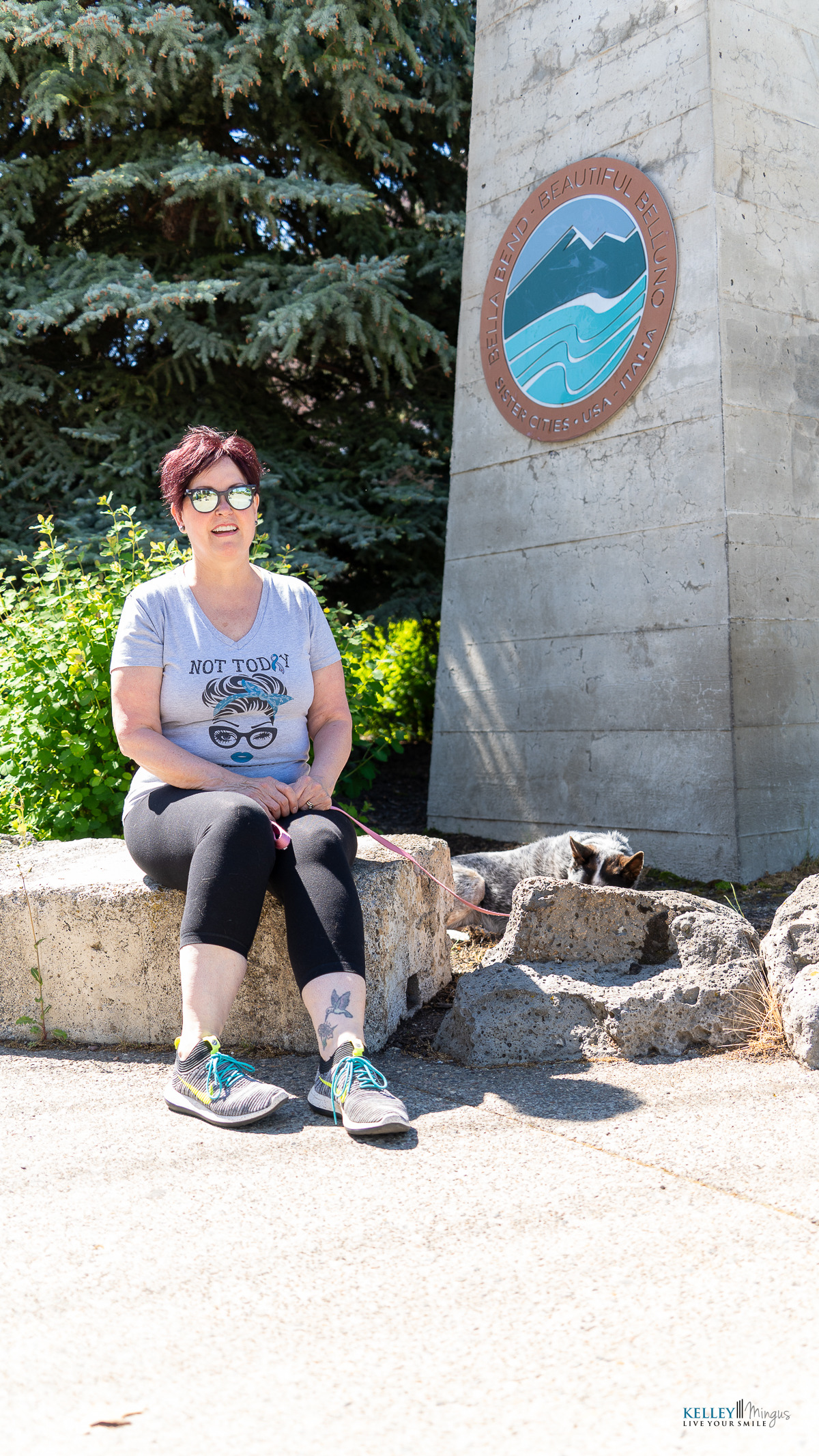 A person wearing sunglasses sits on a stone bench near a concrete marker with a circular "Idaho, This Beautiful Land" emblem, enjoying the outdoors—perhaps reflecting on the benefits of holistic TMJ treatment in such serene surroundings.