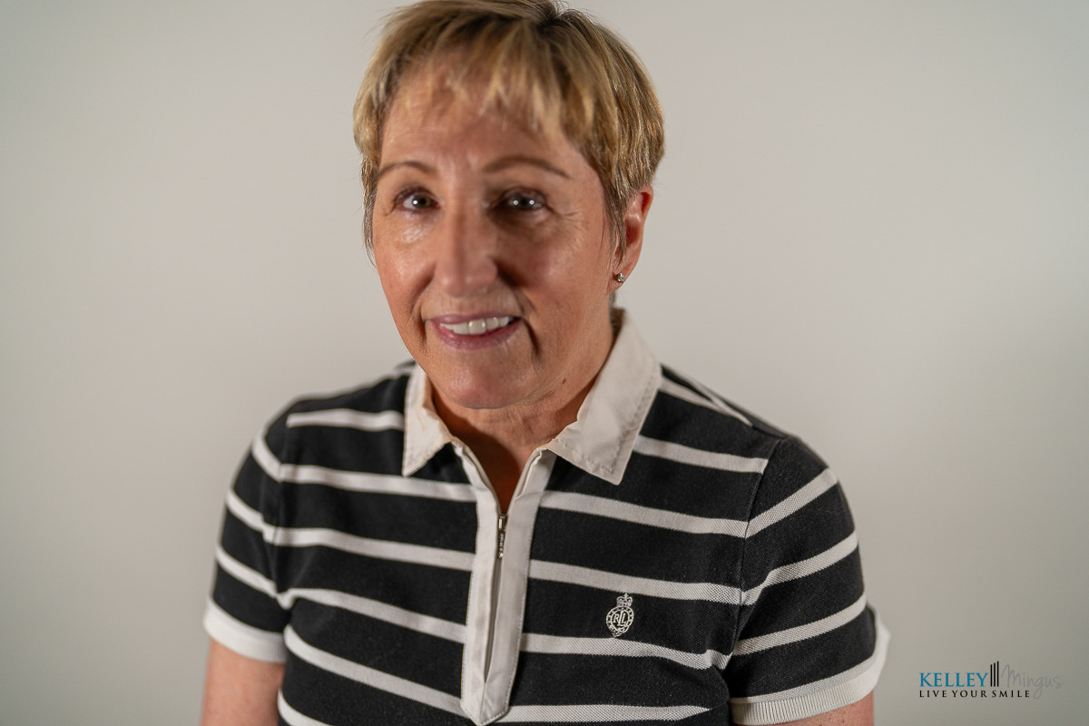 Smiling woman with short light brown hair wearing a black and white striped polo shirt, photographed against a plain light background, representing confidence in holistic TMJ therapy options.