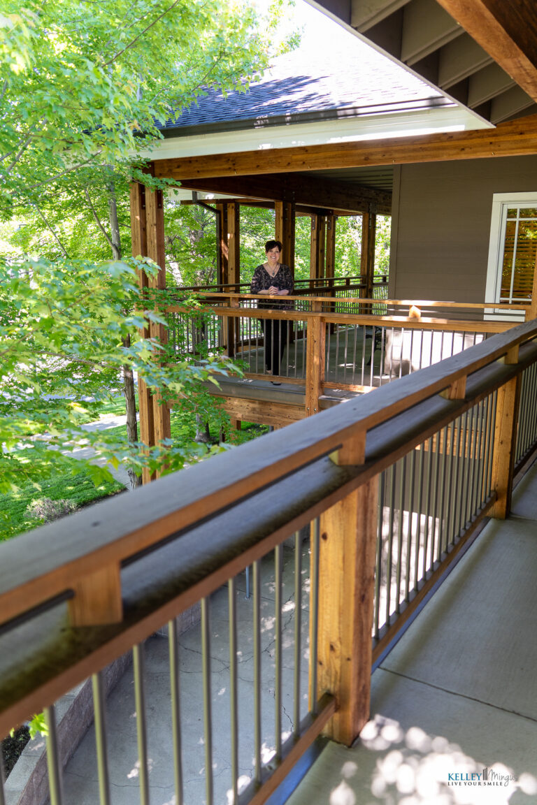 A person stands on a wooden balcony surrounded by green trees, with metal railings and a roof overhead, seeking a moment of calm from challenges like Binocular Vision Dysfunction (BVD) or Temporomandibular Joint (TMJ) disorders.