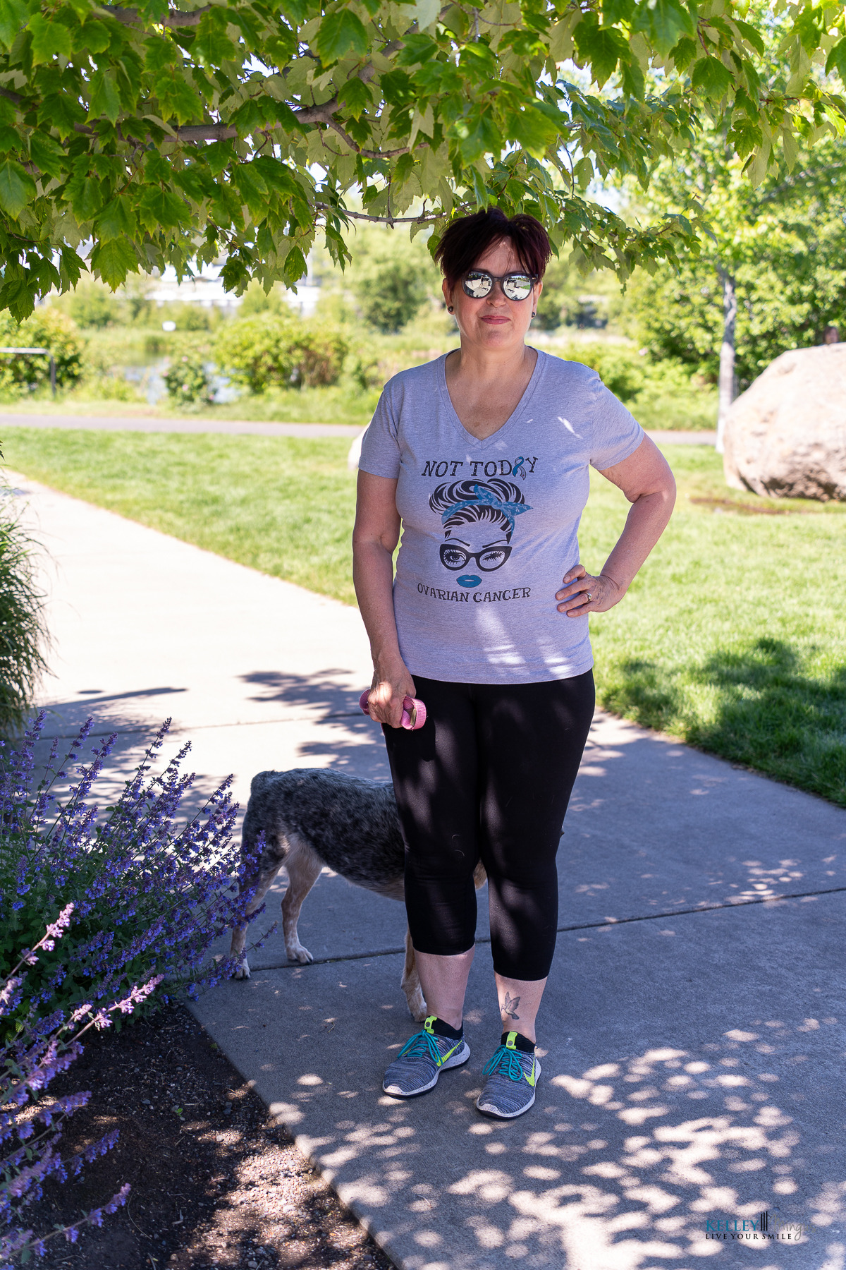 A woman wearing sunglasses and a "Not Today Ovarian Cancer" shirt stands on a park path, holding a pink ball. A dog is partially visible behind her, highlighting the spirit of wellness and holistic sleep apnea treatment.