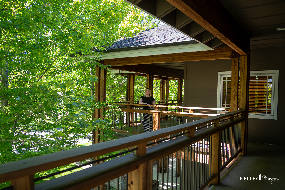 A person stands on the wooden porch of a house surrounded by green trees on a sunny day, enjoying the peaceful atmosphere after a visit to a holistic dentistry clinic.