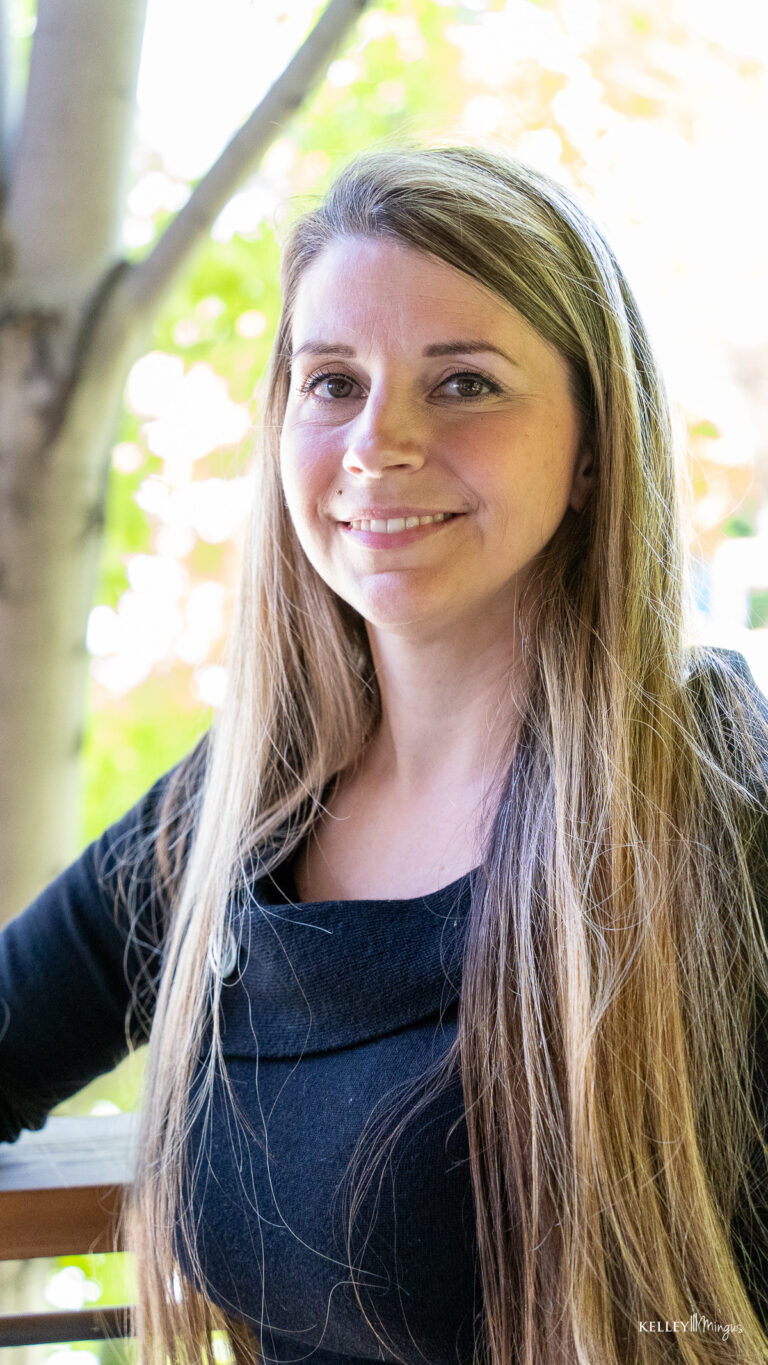A woman with long, straight hair wearing a black top stands outdoors, smiling at the camera with trees blurred in the background—radiating confidence like she just left her family dentist in Bend Oregon.