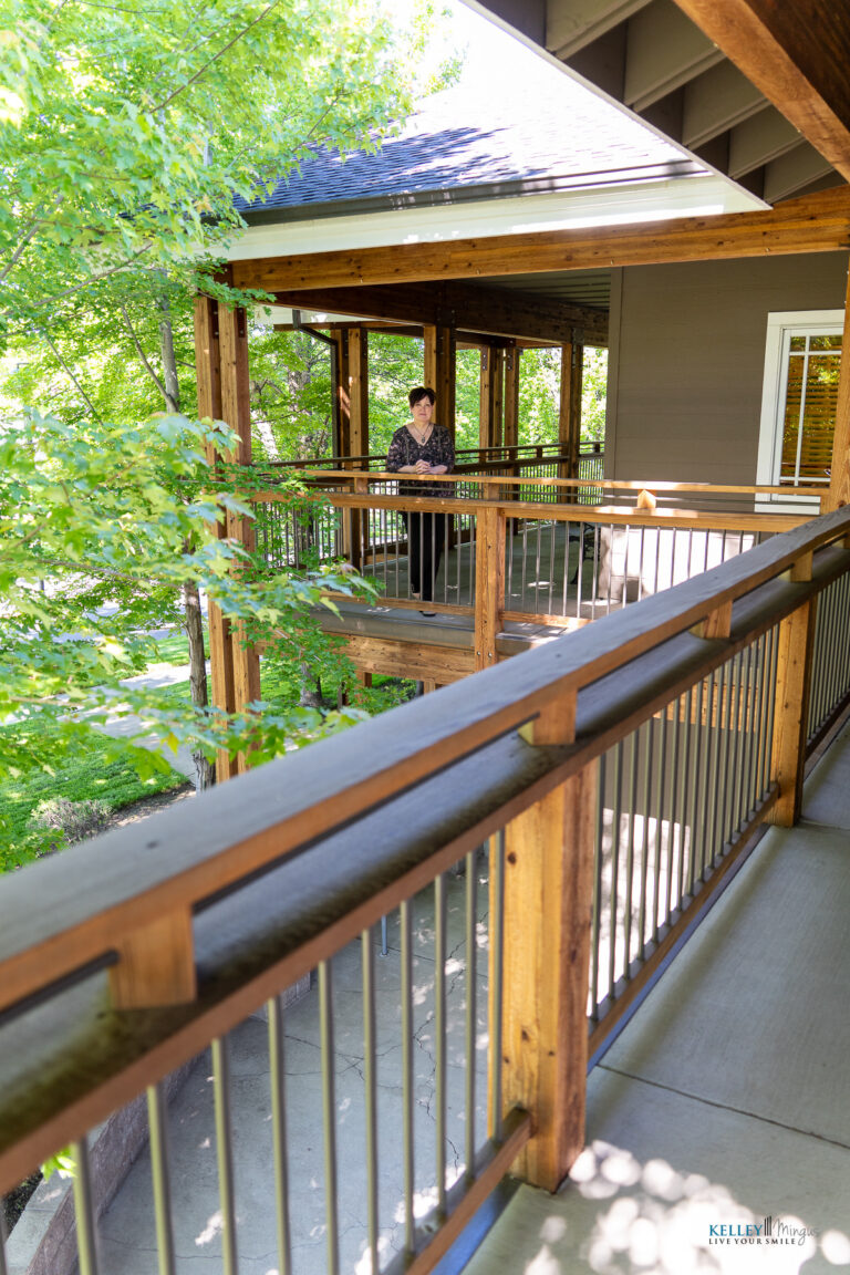 A person stands on a wooden balcony surrounded by trees and greenery, with sunlight filtering through the leaves on a clear day, peacefully enjoying the fresh air—a natural setting reminiscent of exploring CPAP alternatives for sleep apnea to enhance restful nights.