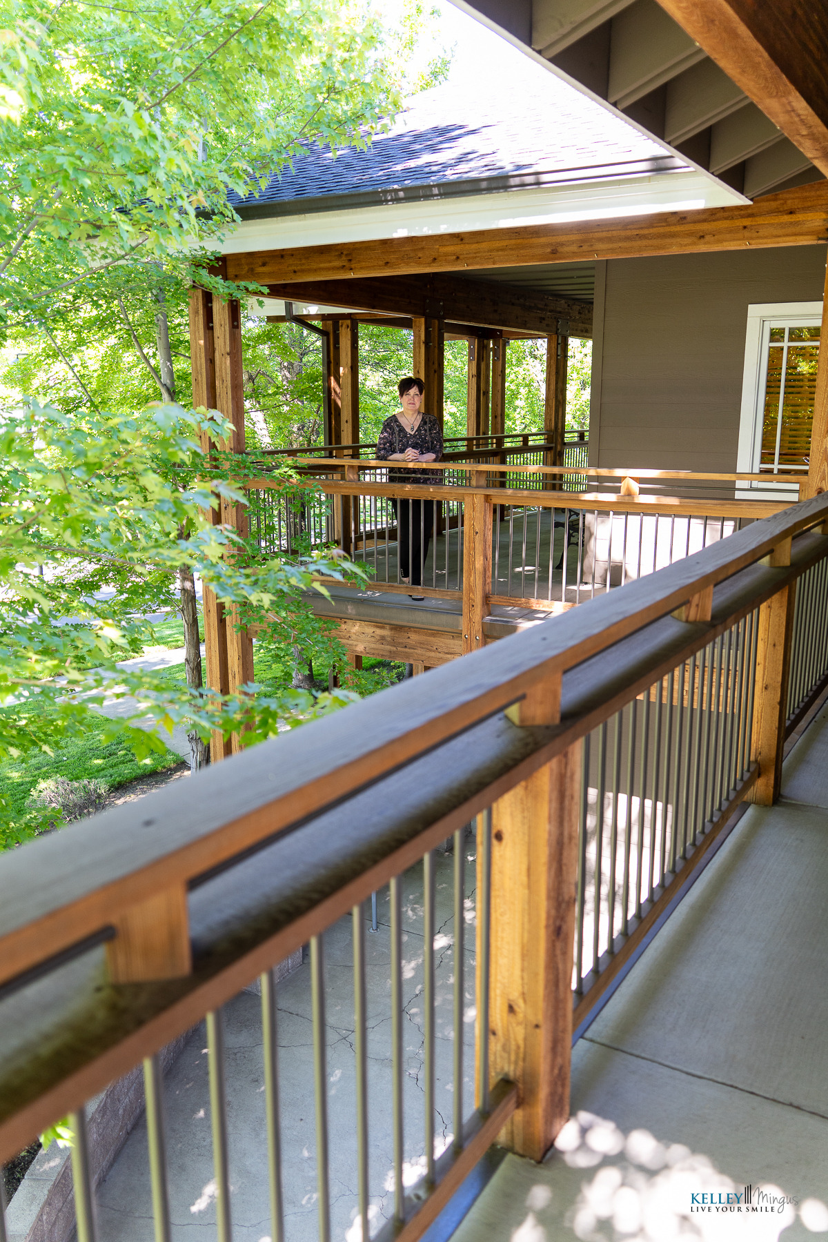 A person stands on a wooden balcony surrounded by trees and greenery, with sunlight filtering through the leaves on a clear day, peacefully enjoying the fresh air—a natural setting reminiscent of exploring CPAP alternatives for sleep apnea to enhance restful nights.