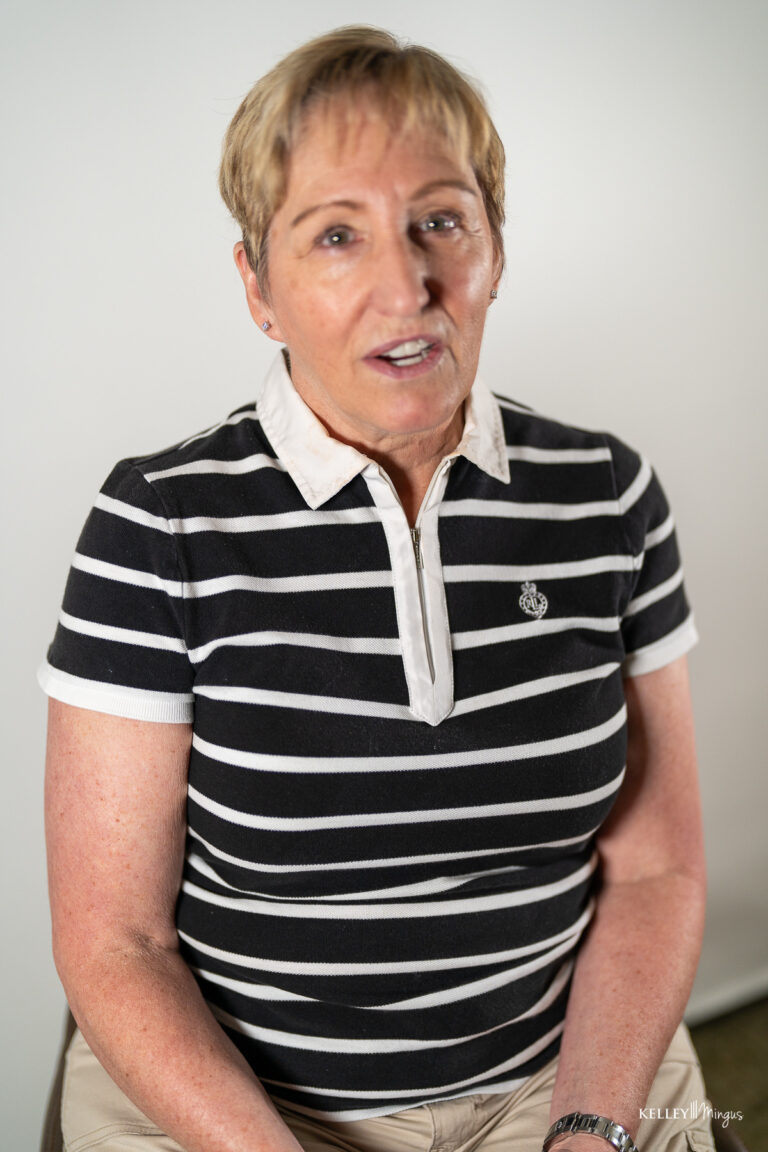 A person with short hair is sitting and wearing a black and white striped polo shirt and beige pants against a plain background, reflecting the calm confidence often seen in those who have experienced Full Mouth Rehabilitation in Bend Oregon.