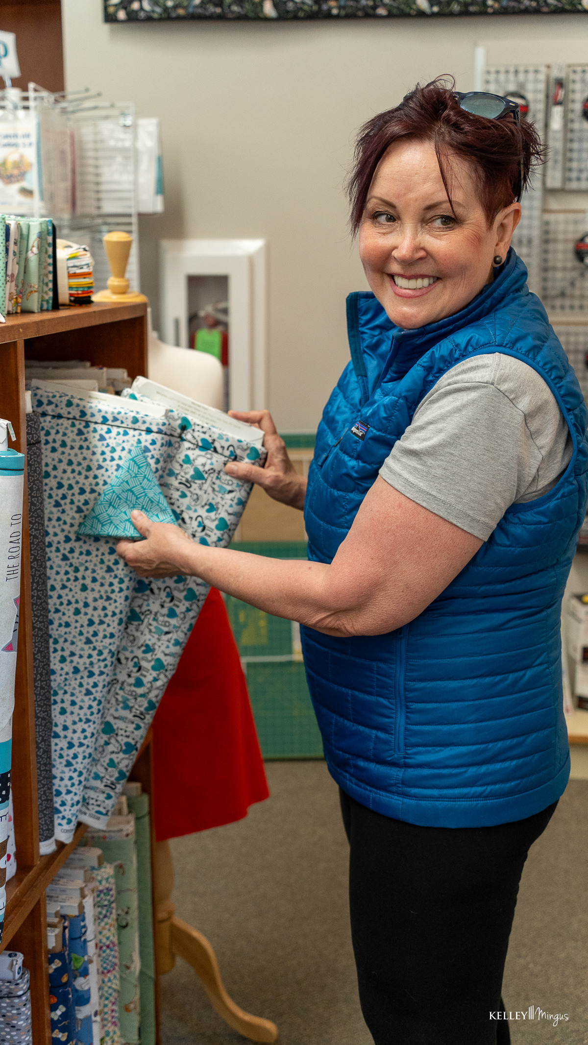 Woman in a blue vest smiles while selecting patterned fabric, exploring CPAP alternatives for sleep apnea in a store.